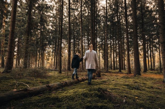Moeder heeft haar zoontje aan de hand die in het bos op een boomstam balanceert.