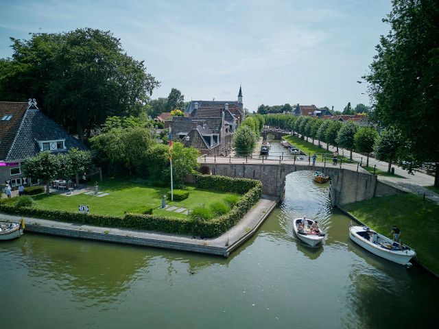 Een sloepje vaart door de gracht in Sloten en is van bovenaf gefotografeerd.