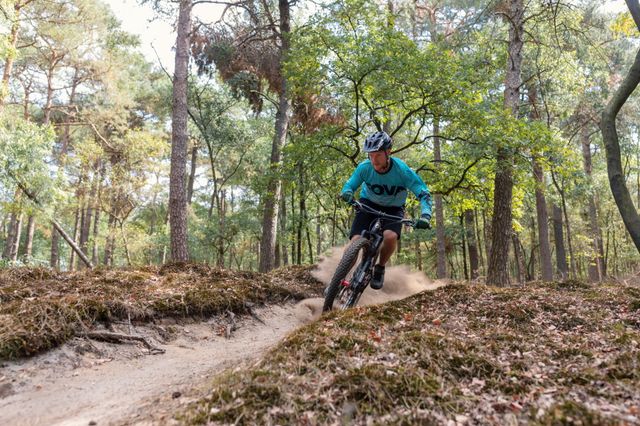 Ein Mountainbiker fährt scharf um die Kurve auf einem Sandweg im Wald.
