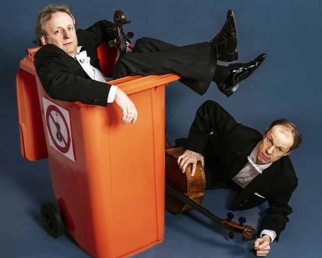 Het Cello duo zit bij een oranje afval kliko