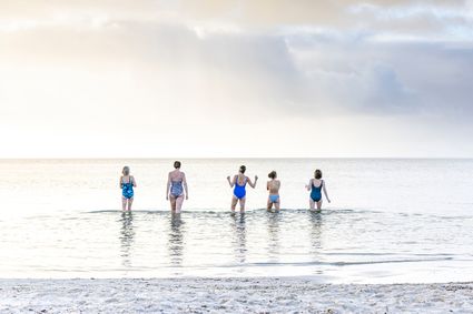 een groep vrouwen loopt naast elkaar het water in