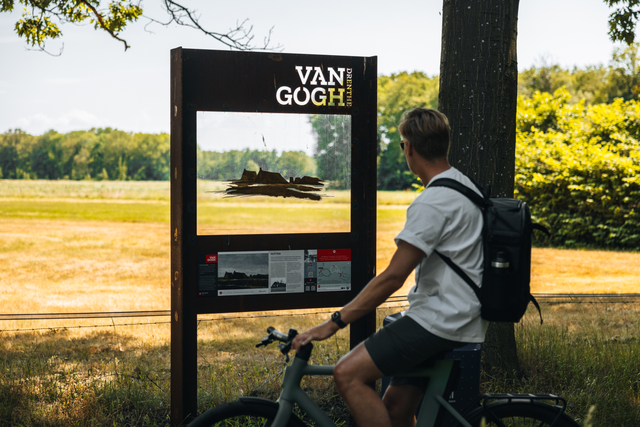 Een man staat stil bij een doorkijkpaneel langs de Van Gogh route waarop het schilderij 'Hutten' te zien is.