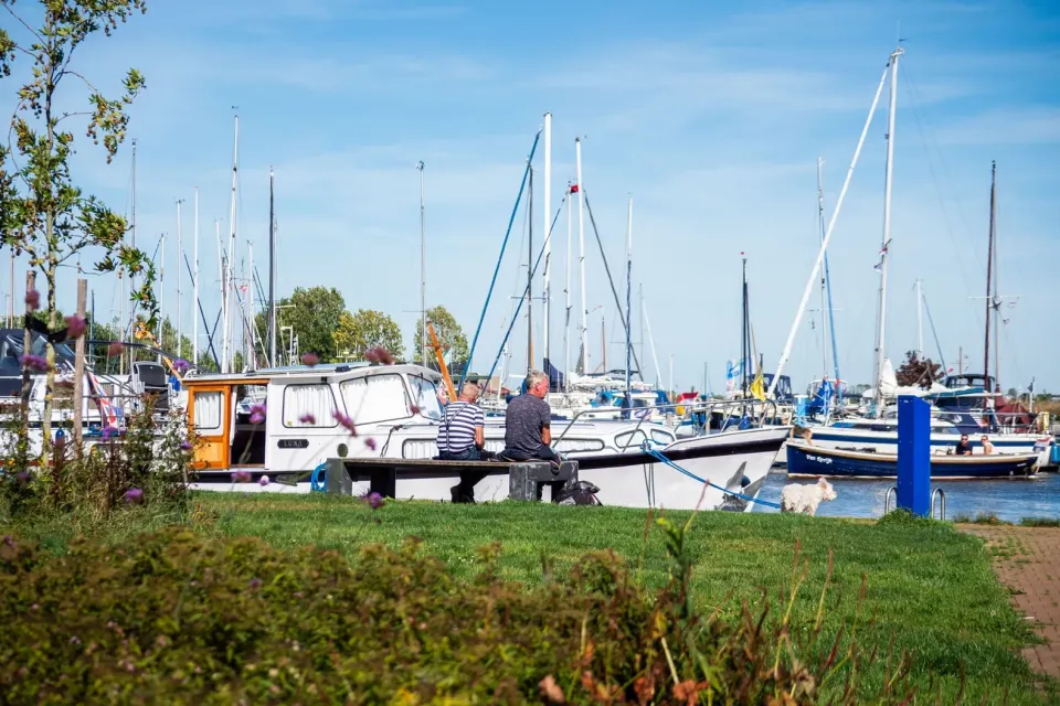 Twee mensen op een bankje met op de achtergrond zeilboten in de jachthaven bij Aquacamping en Jachthaven De Rakken in Woudsend.