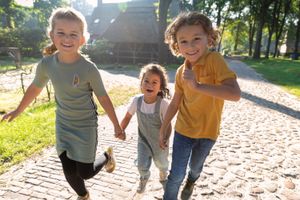 Kinderen rennen hand in hand lachend door een Drents brinkdorp.