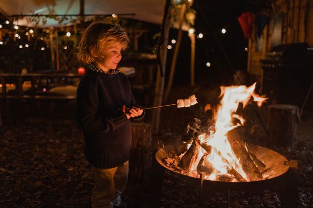 Jongentje staat met marshmallow bij kampvuur.
