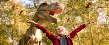 Meisje gooit met herfstbladeren met op de achtergrond een dino