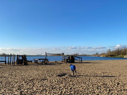 Kinderen spelen in een speeltuin op het strand aan het water.