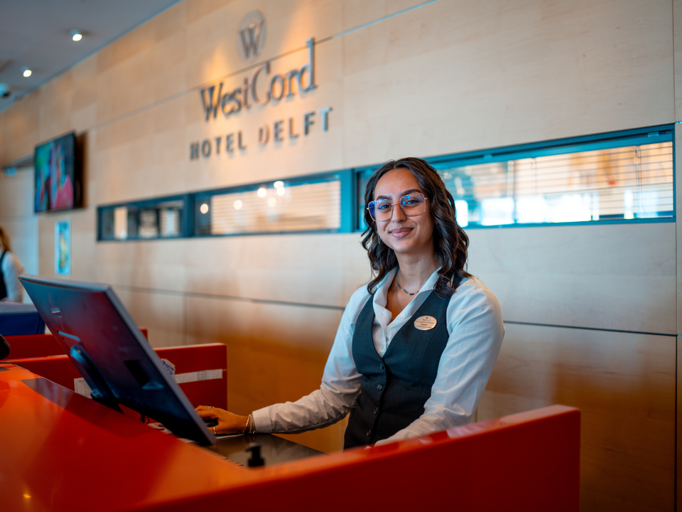 UITvergroot een lachende vrouwelijke receptiemedewerker bij Westcord Hotel Delft