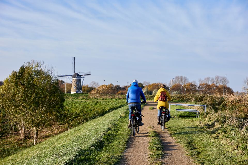 Fietsers over dijk met molen op achtergrond