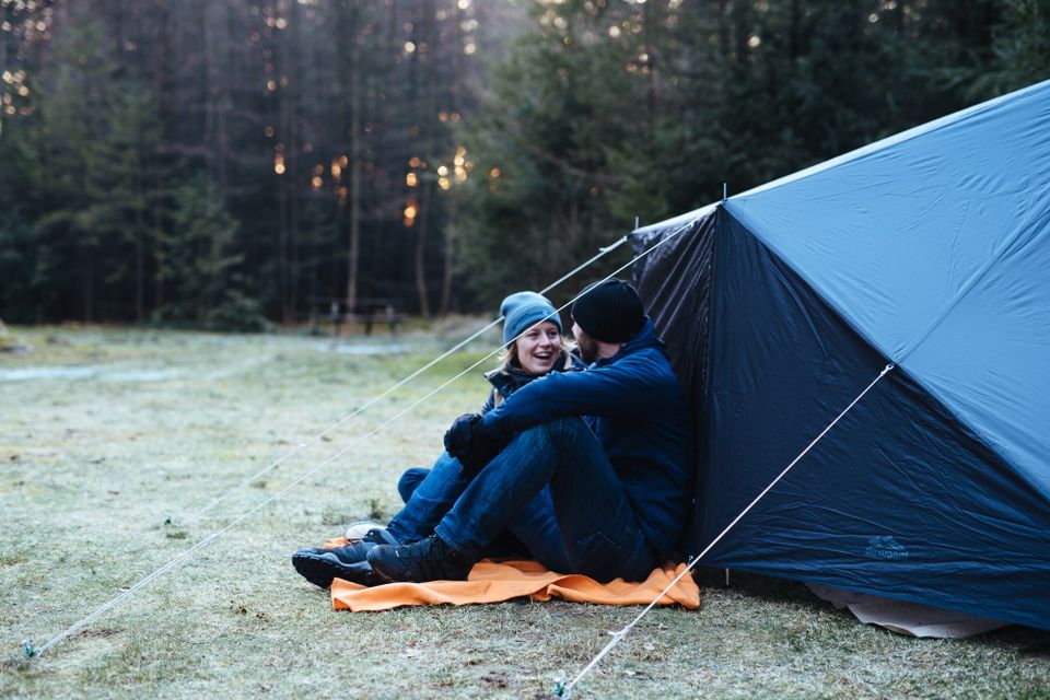 Een man en vrouw zitten warm aangekleed voor een tent op een winterdag.