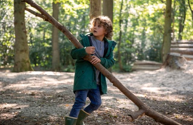 En jongetje sleept met een grote tak door het bos.