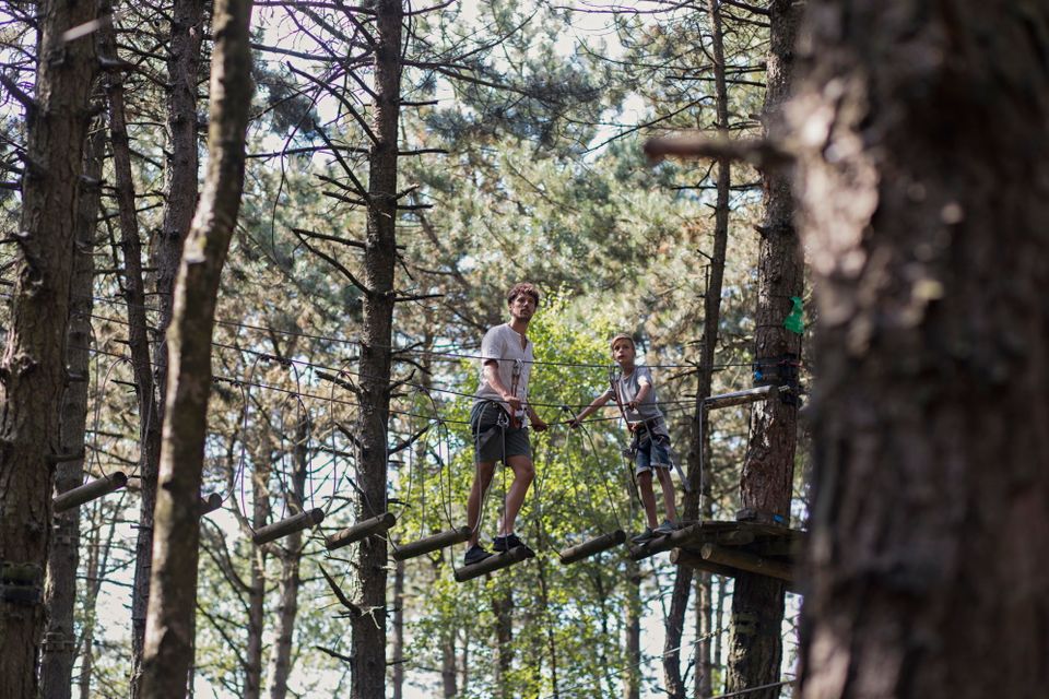 Vader en zoon samen in het klimpark tussen de bomen.