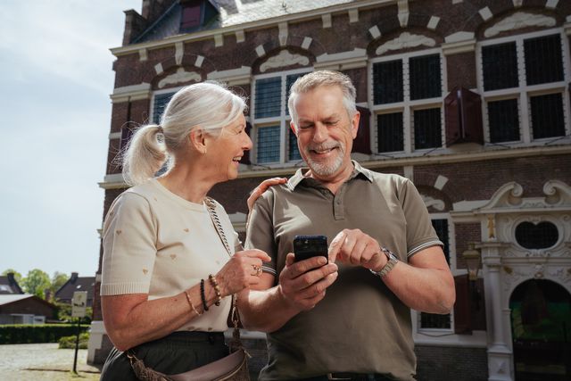 Een man en een vrouw spelen de outdoor escape webapp Ontdek Willemstad op hun telefoon voor het Mauritshuis