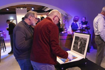 Fototentoonstelling Café Woerden Fotografen, bezoekers bekijken fotowerk in Woerden, Groene Hart, binnenruimte met expositiepresentatie en mensen die foto’s doorbladeren tijdens een culturele bijeenkomst.