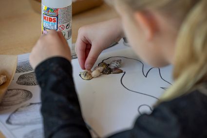 Meisje plakt schelpen op een schilderij met de vorm van een zeepaard erop getekend.