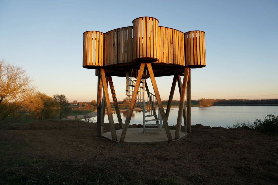 Een uitkijktoren in de vorm van een min of meer ronde fibula met uitstulpingen aan vier kanten kijkt uit over de Loowaard, met water op de achtergrond.