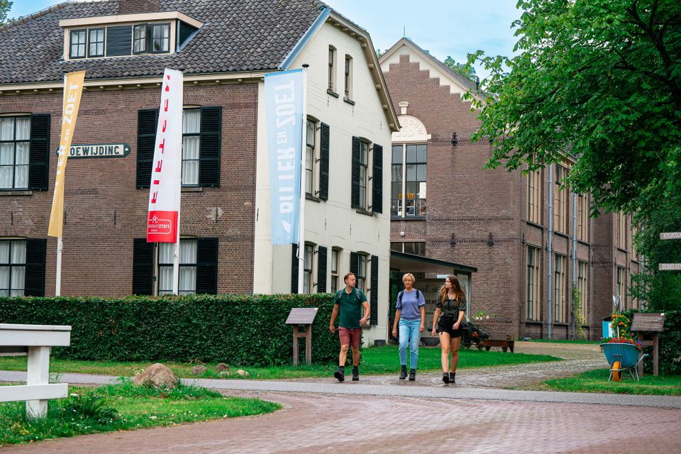 Drie mensen wandelen langs een statig pand in Veenhuizen, voormalig Kolonie van Weldadigheid.