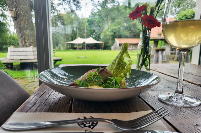 Ein gedeckter Tisch mit einem Glas Weißwein und einem schön präsentierten Teller mit Essen.