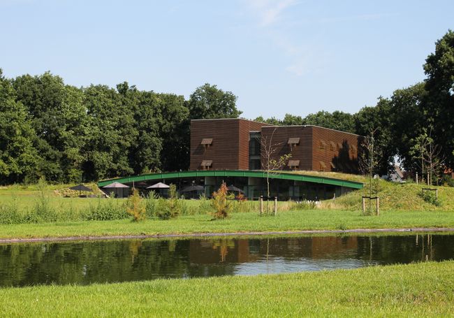 Buitenkant van Boshotel Overberg, omringd door groen en met een vijver op de voorgrond. Het moderne hotel ligt in een rustige, natuurlijke omgeving op de Utrechtse Heuvelrug.