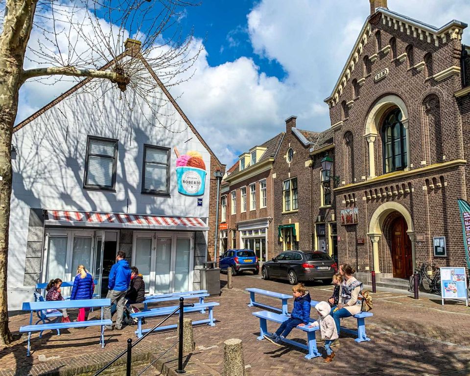 Buitenaanzicht van IJssalon Roberto in pittoresk Oudewater met blauwe bankjes ervoor waarop mensen en kinderen zitten.