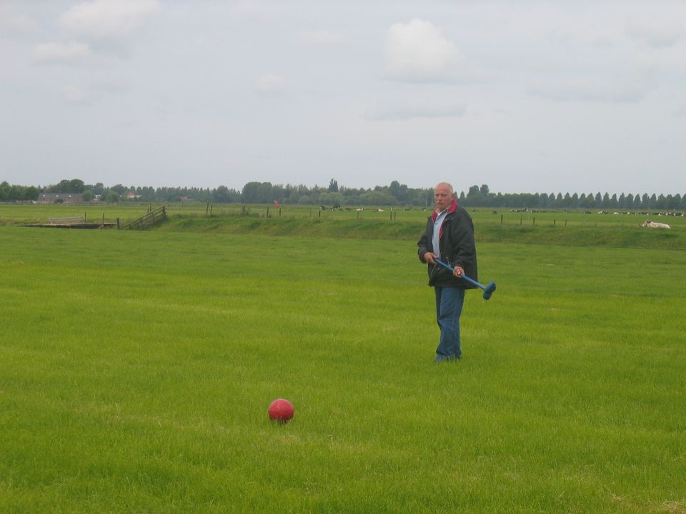 Groepsactiviteit klompengolf bij Boer Hans in Montfoort, Groene Hart, speler met klompengolfclub en rode bal in het open polderlandschap met weilanden op de achtergrond.