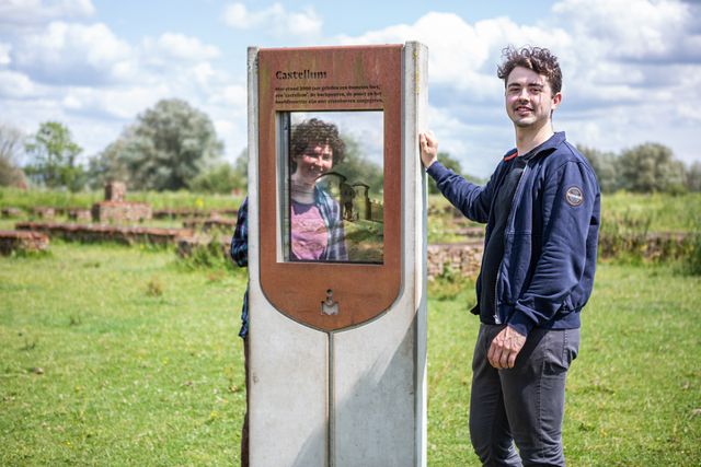 Een jonge man en vrouw kijken door een kijkvenster bij castellum Meinerswijk.