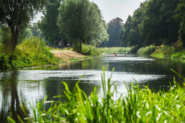 Recreanten fietsen en kanoën langs een groene watergang in Leusden. De foto laat zien hoe fietsen, natuur en recreatie op het water samenkomen in het landelijke buitengebied.