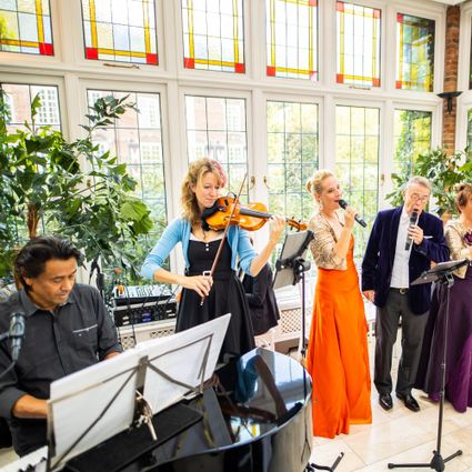Foto van muziekensemble met van links naar rechts een pianist, een violiste, een zangeres en een zanger, allen in stijlvolle, gekleurde galakleding.