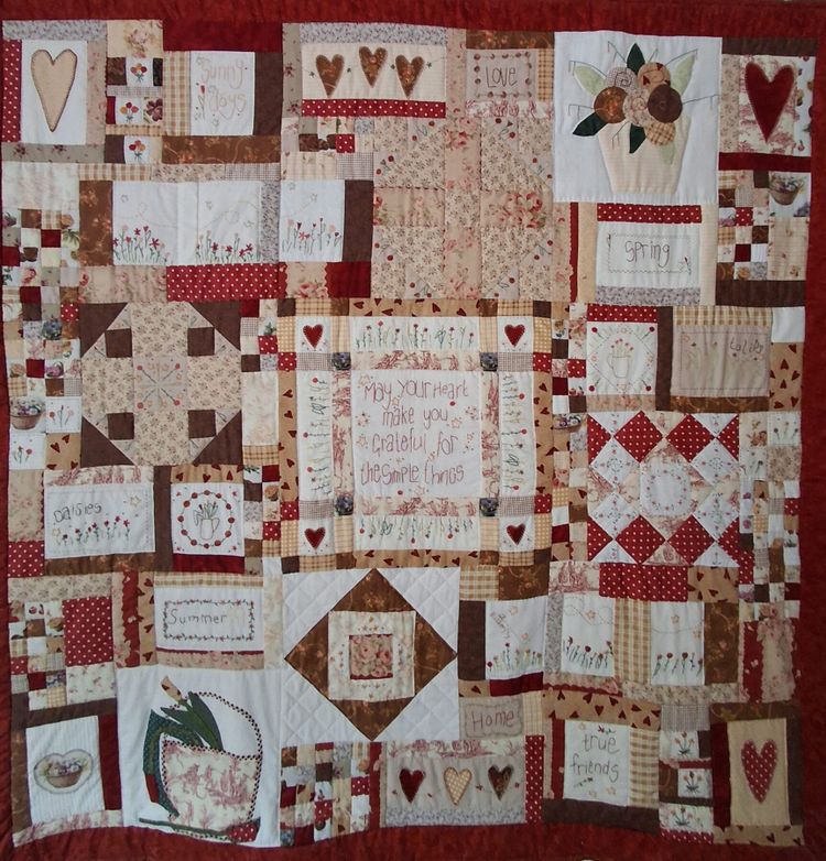 Foto van een quilt van lapjes stof in rood-wit-zand kleuren met verschillende dessins.