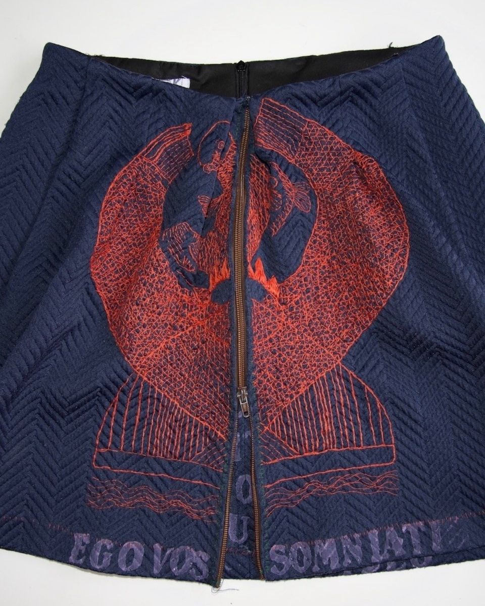 Donkerblauwe handgemaakte rok met rood borduursel en tekst “Ego Vos Somniate”, onderdeel van een textielkunstwerk binnen de expositie.