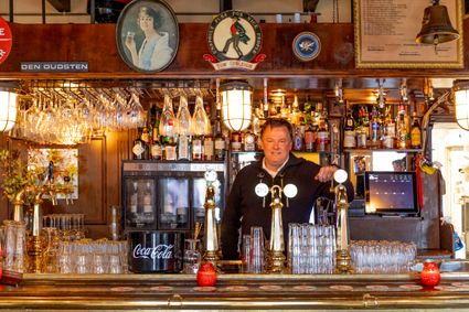 Café de Pompier in Woerden, regio Groene Hart, horecalocatie met terras en glazen pui voorzien van rode banner en slogan, vastgelegd tijdens de 40-jaar-reünie bij deze bekende uitgaansgelegenheid in het centrum.
