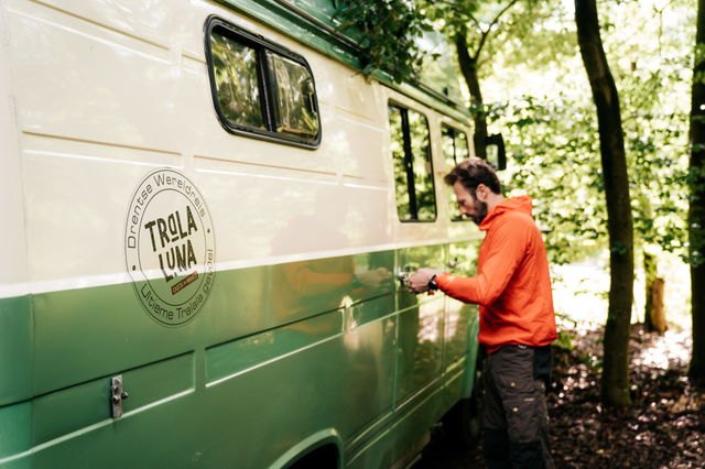 Een man opent de deur van een groen/wit retrobusje van Tralaluna Casita on Wheels.