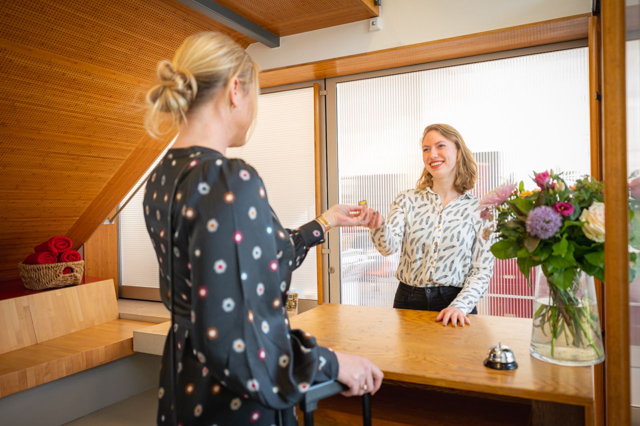 Medewerker bij de receptie geeft iets aan de gast