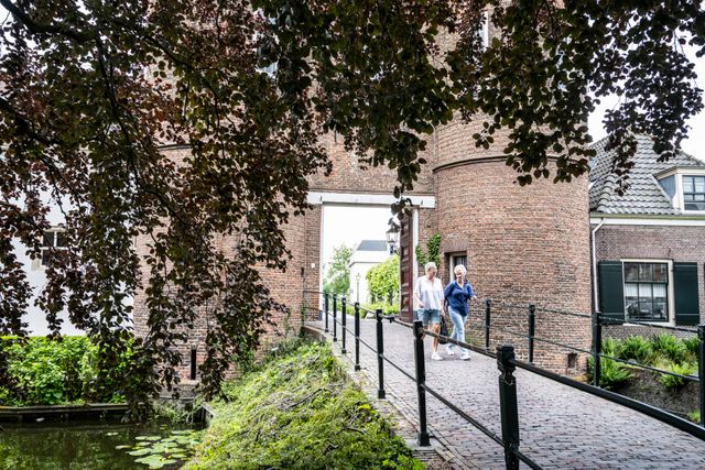Historisch kasteel Kasteel Montfoort in Montfoort, Groene Hart. Bezoekers wandelen over de brug door de monumentale poort, omringd door de gracht, oude bakstenen muren en groene bomen.