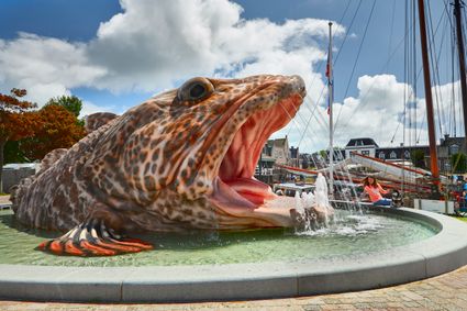 vis fontein van stavoren van de zijkant.
meisje zit op de rand van de fontein met haar hand in het water.