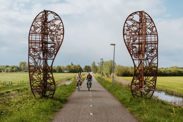 Twee fietsers op het Halve Zolenpad bij het kunstwerk met twee grote schoenen.
