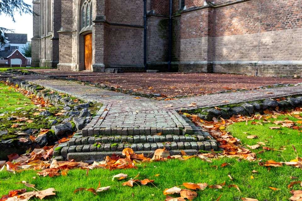 Herfstbladeren liggen in het gras. Uit het gras komen de bakstenen contouren van een tempel. de kerk op de achtergrond.