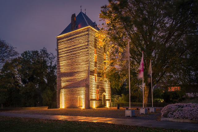 De Kasteeltoren van IJsselstein verlicht in het donker, omgeven door bomen en vlaggen, een historisch icoon midden in het Groene Hart.