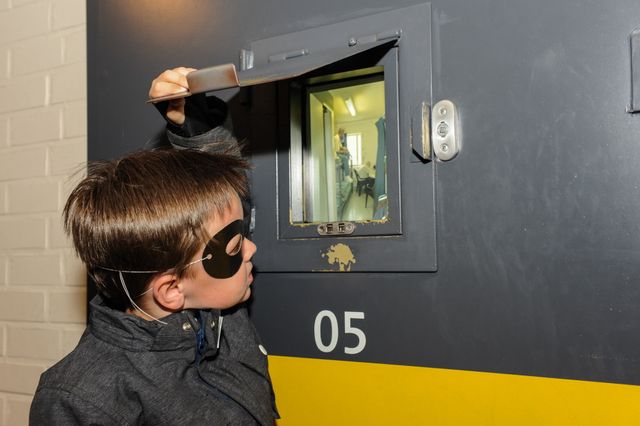 Een jongetje met boevenmasker op kijkt door een celluikje in het gevangenismuseum.