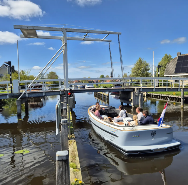 Sloep met passagiers vaart onder een brug in Woudsend in Zuidwest Friesland.