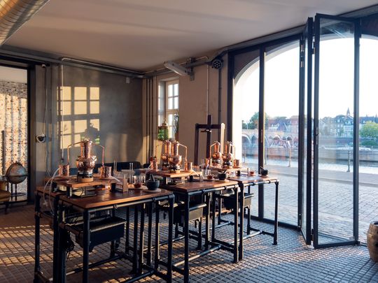 Ambachtelijke ginworkshop bij Het Stookatelier in Maastricht met uitzicht op de Maas. De koperen distilleerketels staan klaar op houten werkbanken in een sfeervolle ruimte aan de Oeverwal 8.