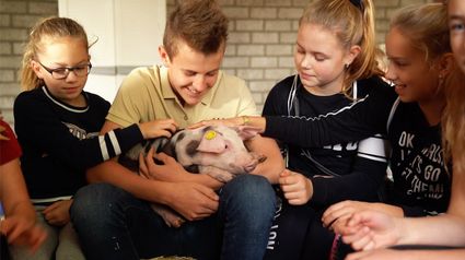 Kinderen die knuffelen met een biggetje.