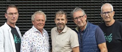 Vijf volwassen mannen staan naast elkaar en kijken in de camera. Ze dragen casual kleding en staan voor een metalen gevel. De foto oogt als een informeel groepsportret, mogelijk van collega’s of bestuursleden.