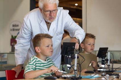Schelpenexpert Hans Post helpt twee kinderen met wat er te zien is op hun microscoop