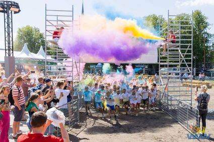 Evenement Color Run Woerdense Vakantieweek in Woerden, Groene Hart. Deelnemers rennen door een startboog terwijl kleurrijk poeder de lucht vult, met publiek langs het parcours tijdens een sportief en feestelijk zomerevenement.