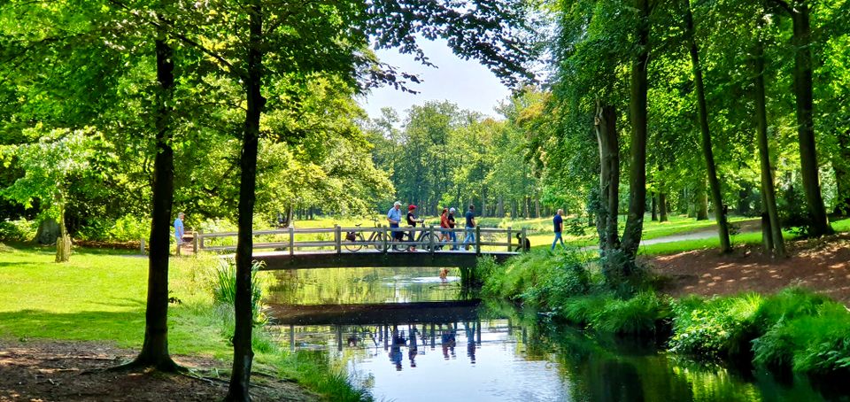 Fietser en wandelaars staan op een brug over een brede sloot middenin het groen