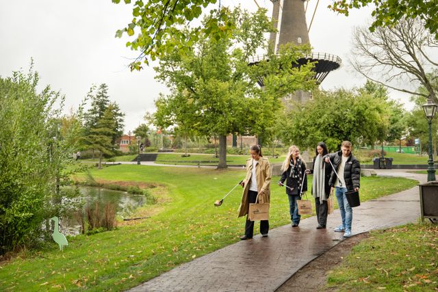 Campagnebeeld van Let's Bloomit, Love Leiden. Vier personen wandelen en gapen afval met grijpers in het Singelpark.