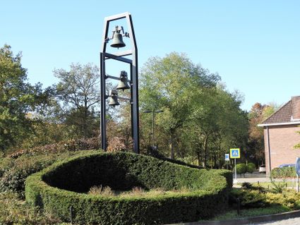 Ein begrünter Kreisverkehr, auf dem ein Metallgestell mit Glocken steht.