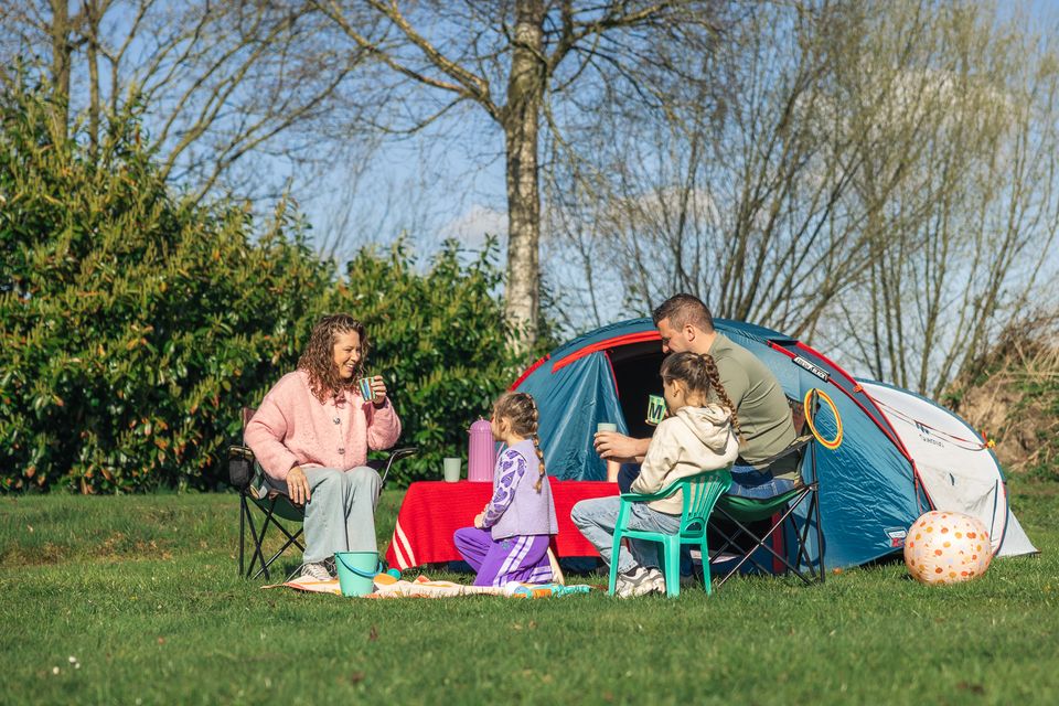 Gezin zit samen voor de tent op Vakantiepark De Leughte bij de Grebbelinie. De foto laat een ontspannen kampeermoment zien met kinderen, buitenleven en vakantie in het groen.