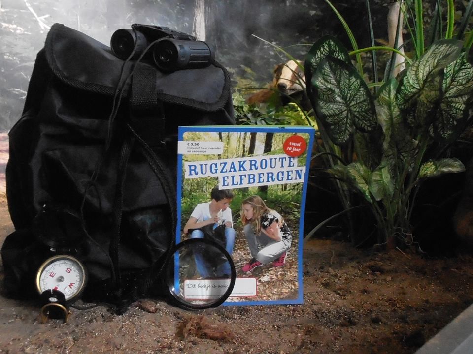 Een zwarte rugzak en het opdrachtenboekje van de Rugzakroute Elfbergen van Mar en Klif.